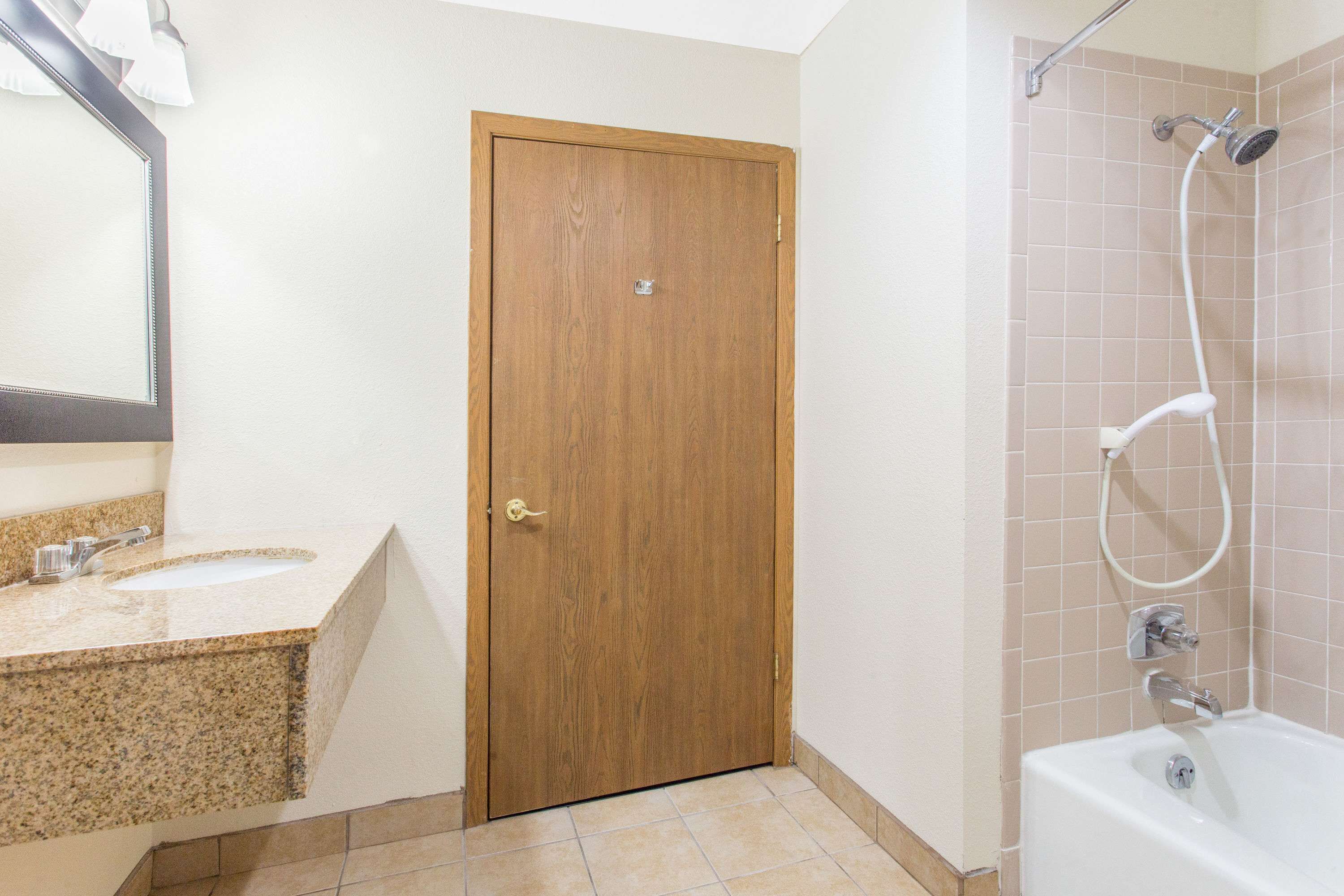 Een badkamer met een houten deur, een wastafel met aanrechtblad en een douchegedeelte met bad.