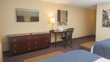 A hotel room with a desk, chair, two beds, a dresser, and a flat-screen TV.