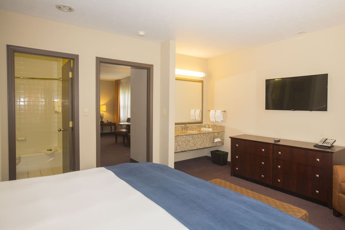 A hotel room with a bed, a bathroom with a shower, a desk, a dresser, and a TV.