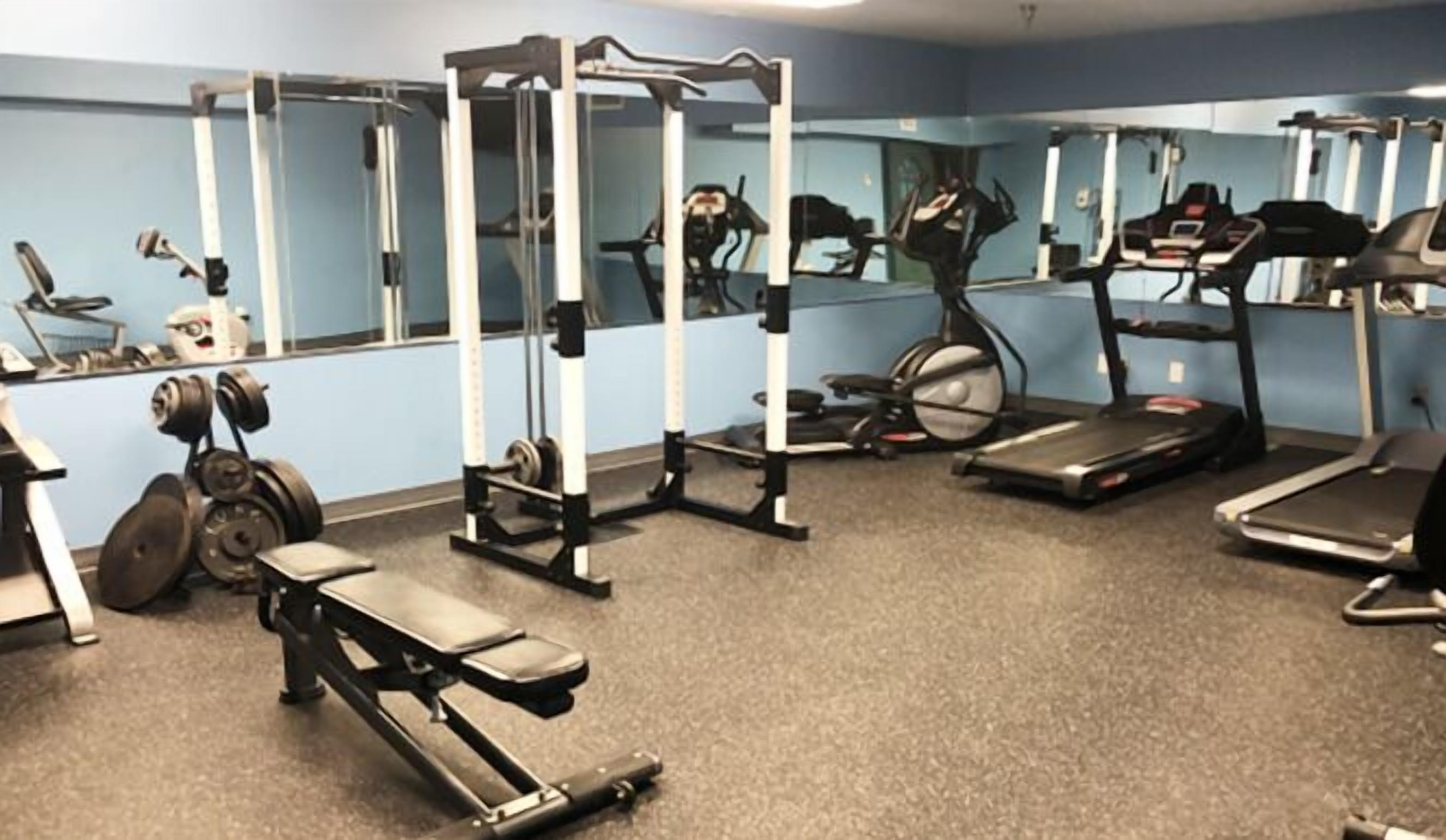 A gym with various exercise equipment including a bench press, a squat rack, treadmills, and a stationary bike.