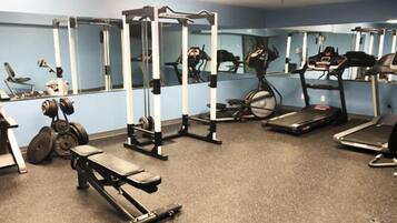 A gym with various exercise equipment including a bench press, a squat rack, treadmills, and a stationary bike.