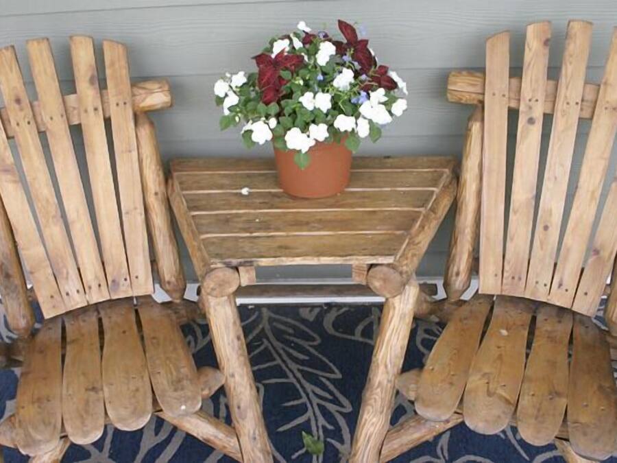 Two wooden Adirondack chairs with a small table and a potted plant between them.