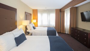 A hotel room with two beds, a TV, a dresser, and a window with curtains.