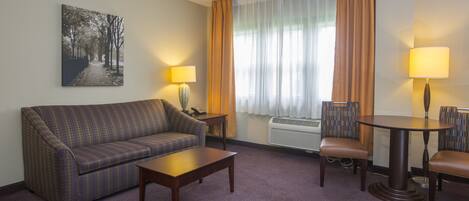 A hotel room with a sofa, a small table, two chairs, a lamp, and a painting on the wall.