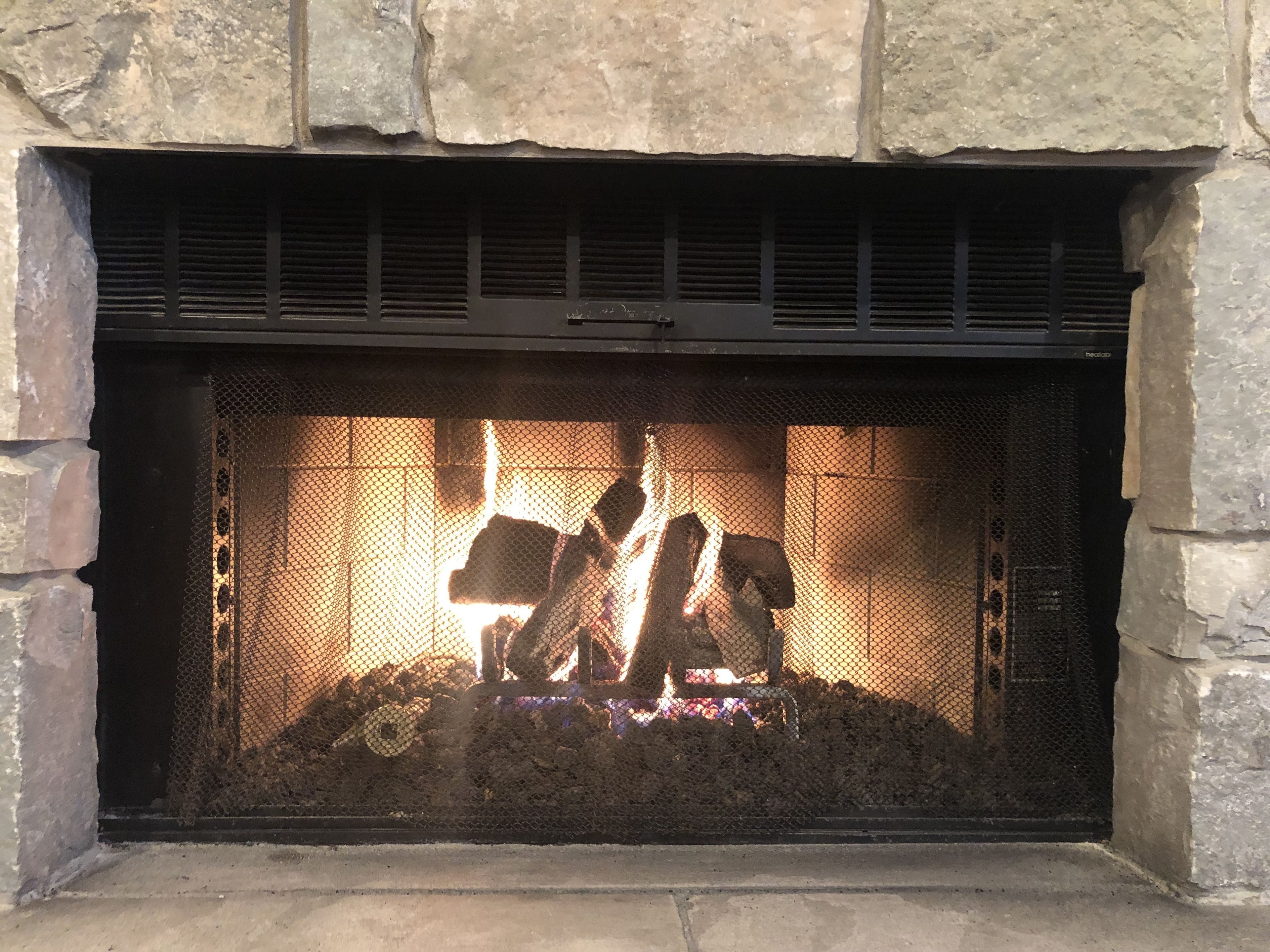 Une cheminée en pierre avec un foyer en métal et un feu qui crépite à l’intérieur.