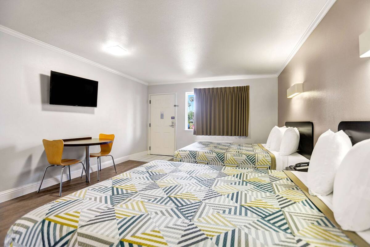 A hotel room with two beds, a desk, and chairs.