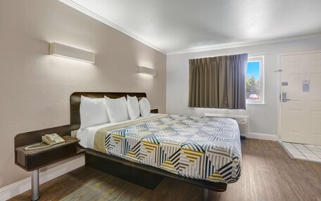 A hotel room with a bed, bedside table with a phone, a window with curtains, and a door.