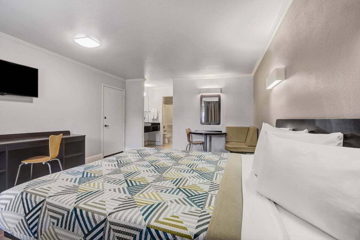 A hotel room with a bed, a desk, a chair, and a TV.