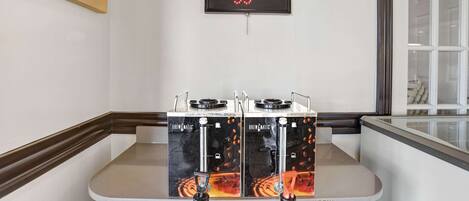 A coffee station with two Brewmatic coffee machines, a neon coffee sign, and a framed 'RISE & SHINE' sign.