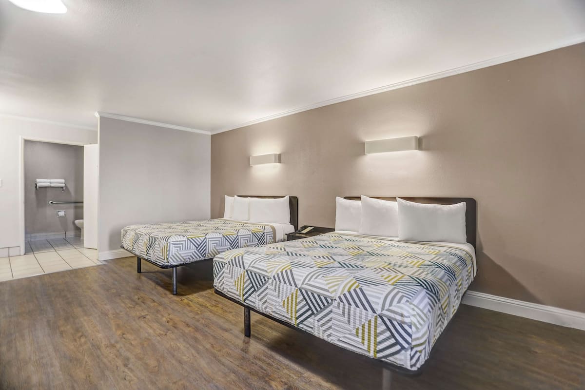 A hotel room with two beds, a wooden floor, and a bathroom visible through an open door.