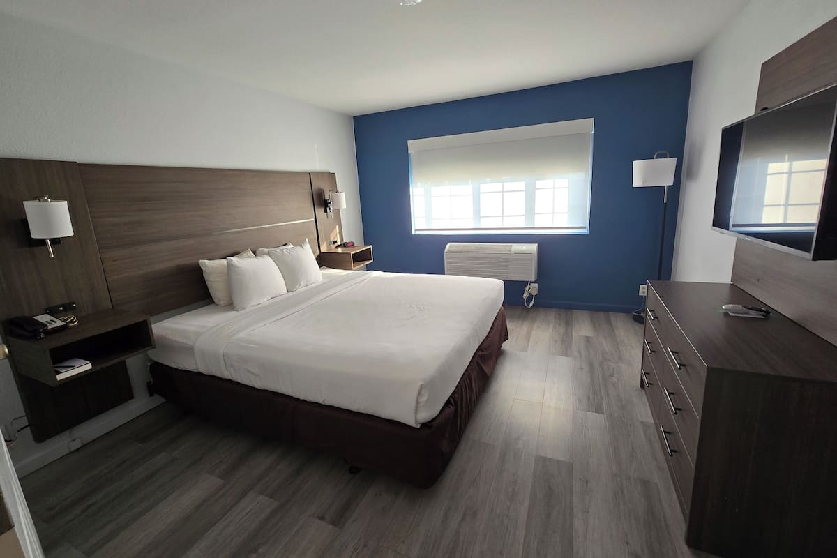 Una habitación de hotel moderna con una cama grande, una mesita de noche con lámpara, un aparador y un televisor.
