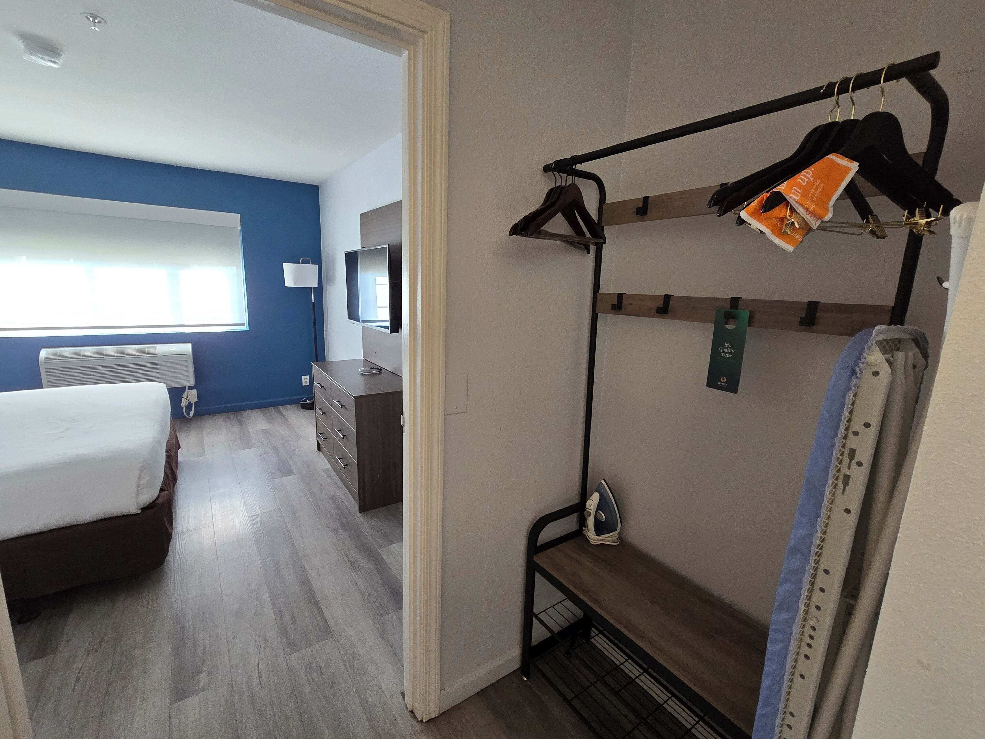 Une chambre d’hôtel équipée d’un lit, d’une commode, d’une télévision et d’un portant à vêtements avec des cintres.
