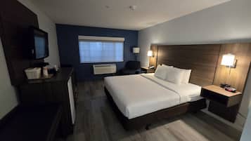 A hotel room with a bed, a desk, a chair, a TV, a lamp, and a nightstand with a clock.