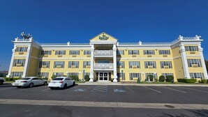 Un grand bâtiment jaune, doté d’une entrée centrale, de nombreuses fenêtres et d’un parking où se trouvent deux voitures.