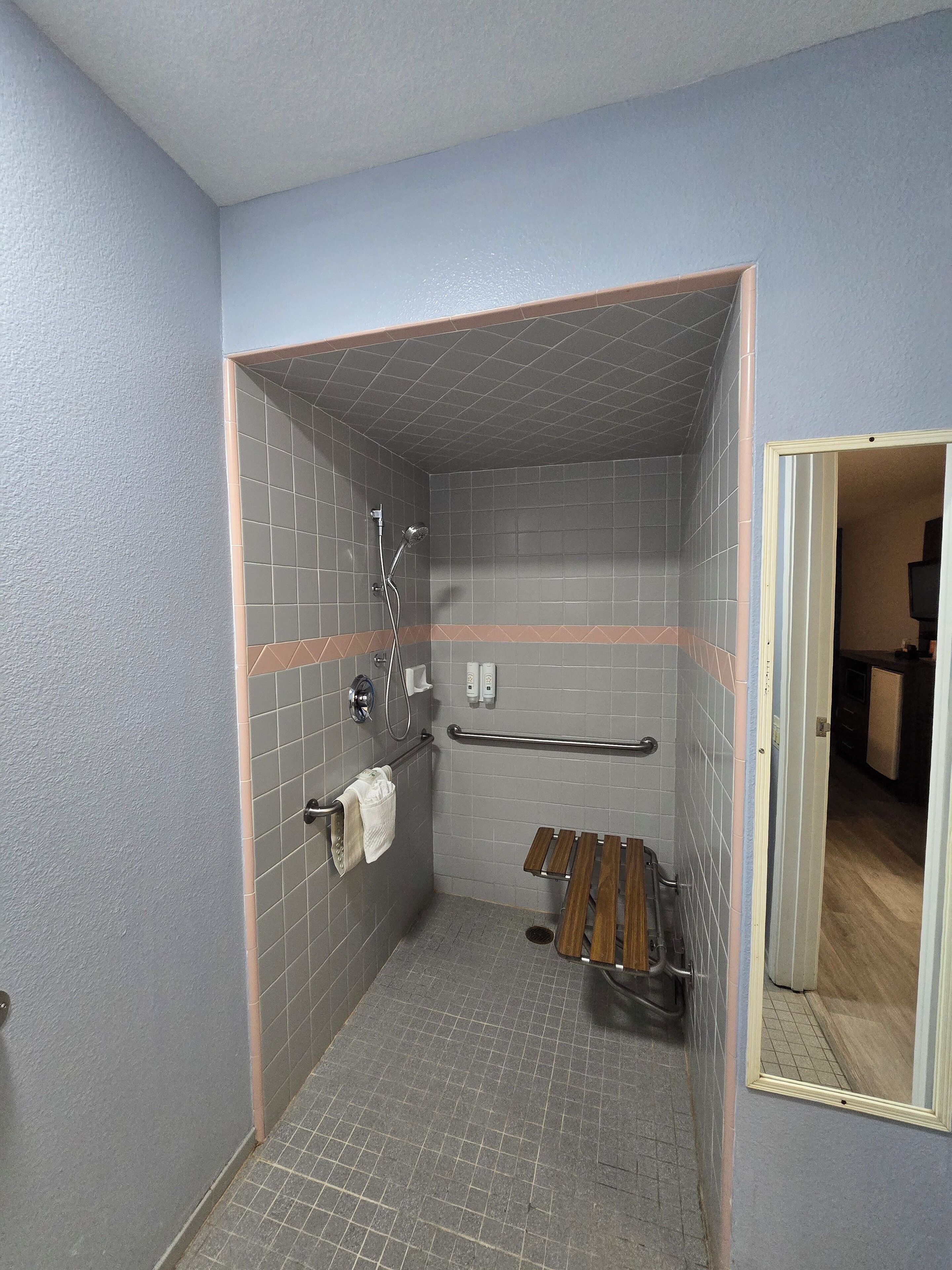 Un espacio de ducha pequeño y cerrado con suelo y paredes de azulejos, un cabezal de ducha manual, un perchero para toallas y un banco de madera.