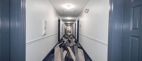 A hotel hallway with a patterned carpet, white walls, and blue doors.