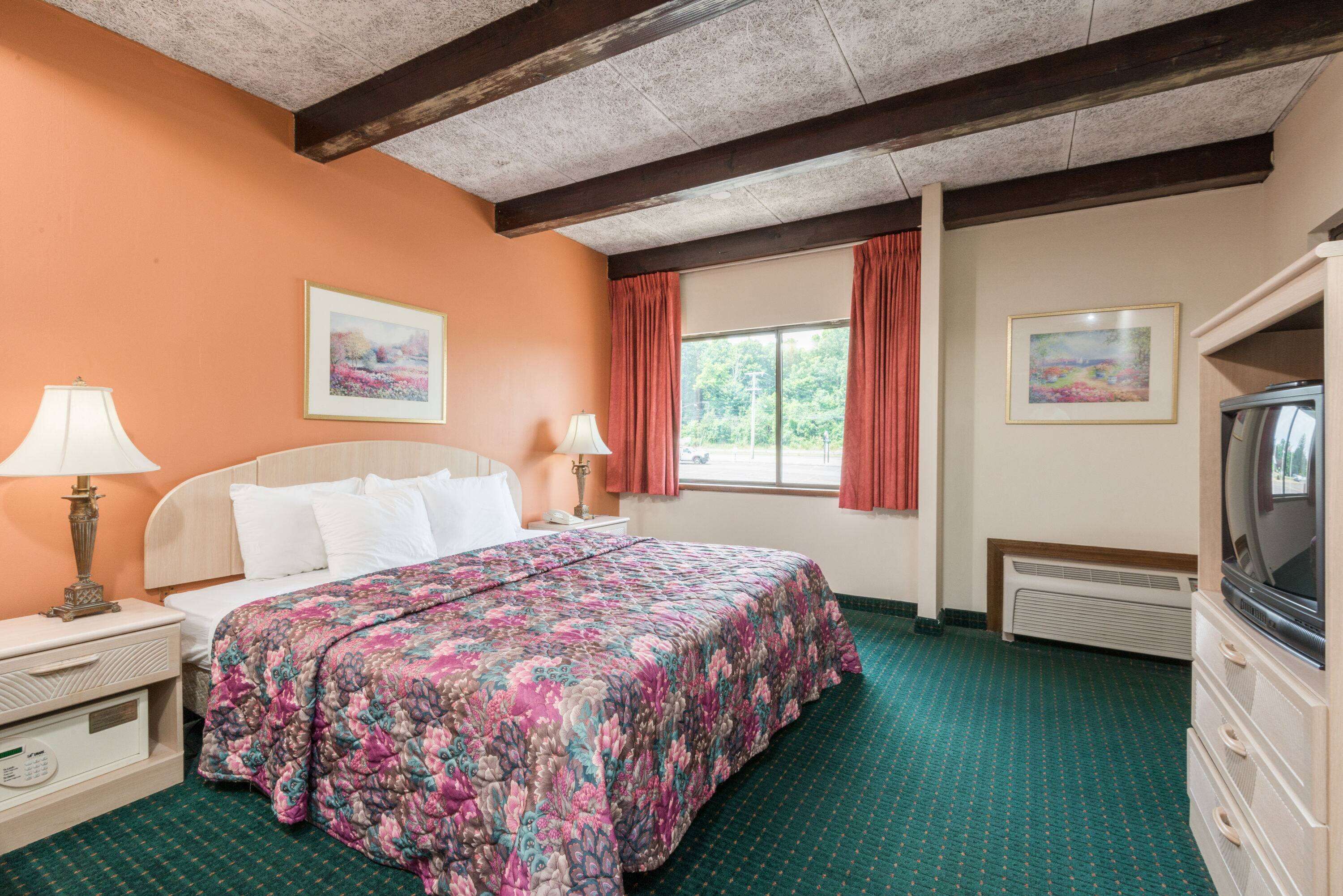 Una habitación de hotel con cama, cómoda, televisor y ventana con cortinas.