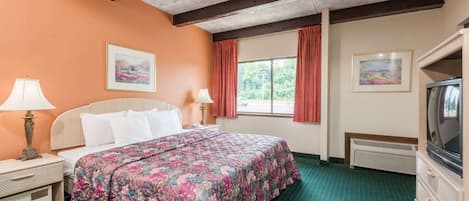 Una habitación de hotel con cama, cómoda, televisor y ventana con cortinas.