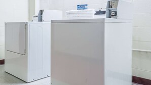 Two white front-loading washing machines in a laundry area with a white tiled wall and a red baseboard. - Days Inn by Wyndham Berlin Meriden (Berlin)