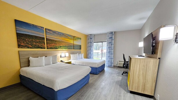 A hotel room with two beds, a desk with a computer, a TV, and artwork on the wall. - Days Inn by Wyndham Berlin Meriden (Berlin)