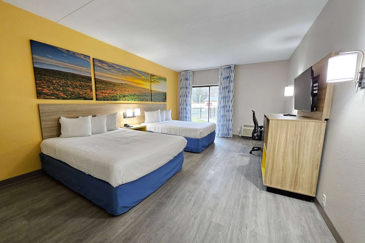 Une chambre d’hôtel avec deux lits, un bureau avec un ordinateur, une télévision et des œuvres d’art accrochées au mur.