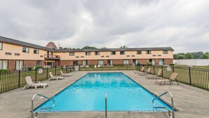 A rectangular pool with metal railings, surrounded by lounge chairs and a brick building with multiple windows and balconies. - Days Inn by Wyndham Berlin Meriden (Berlin)