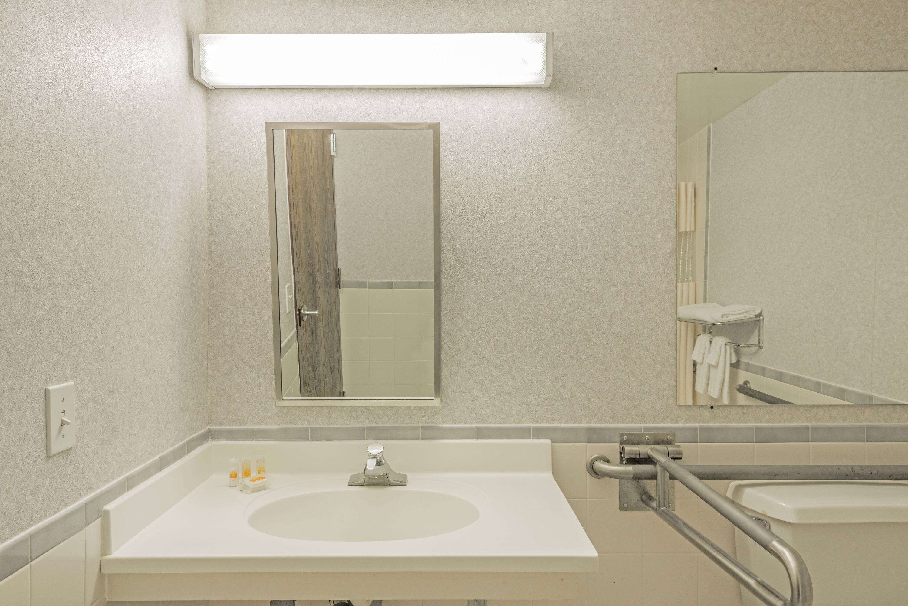 A bathroom with a white sink, a mirror, and a handrail.