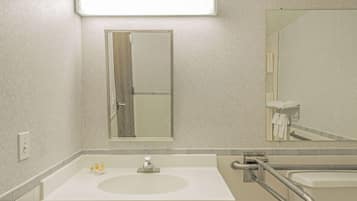A bathroom with a white sink, a mirror, and a handrail.