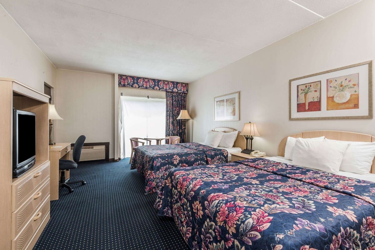 Une chambre d’hôtel avec deux lits, un bureau avec une télévision, une chaise, une lampe et une fenêtre avec des rideaux.