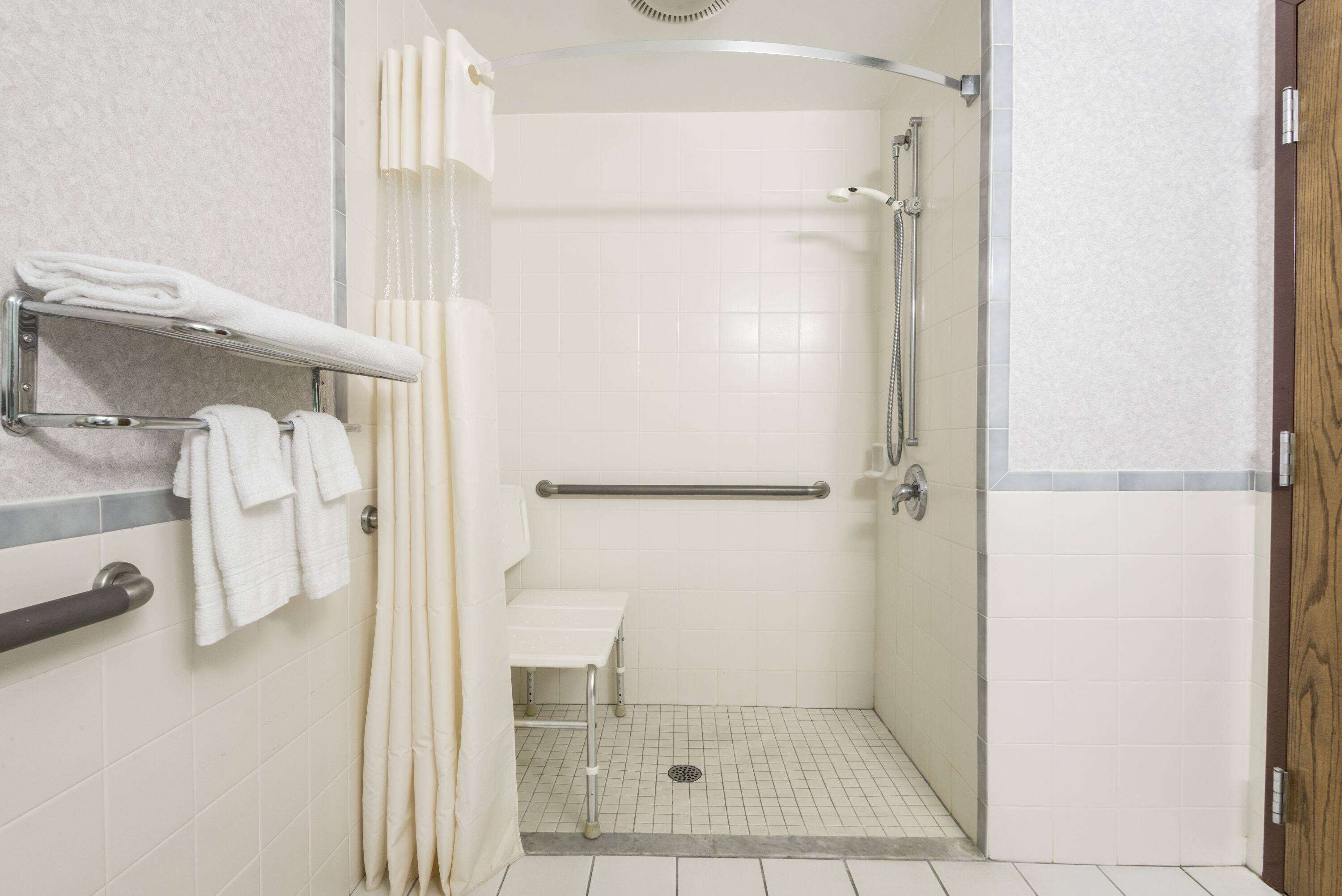 A walk-in shower with a grab bar, a bench, and a towel rack.