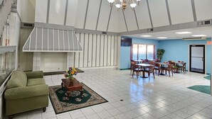 A spacious lobby with a high ceiling, a chandelier, a fireplace, and a dining area with tables and chairs. - Days Inn by Wyndham Berlin Meriden (Berlin)