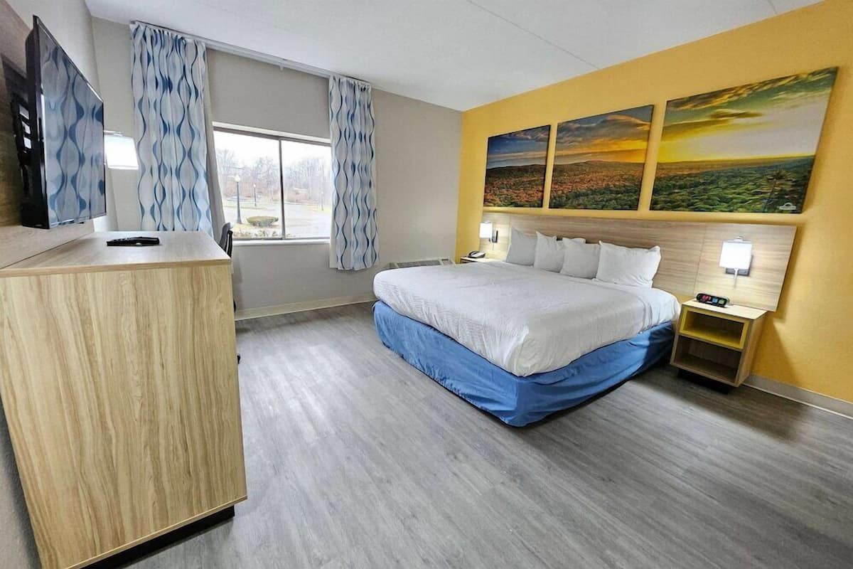 Une chambre d’hôtel avec un lit, un bureau, une télévision et une fenêtre avec des rideaux.