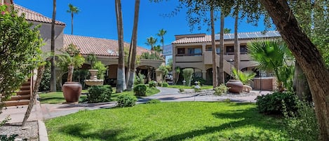 A hotel courtyard with palm trees, a fountain, and a building with a tiled roof.