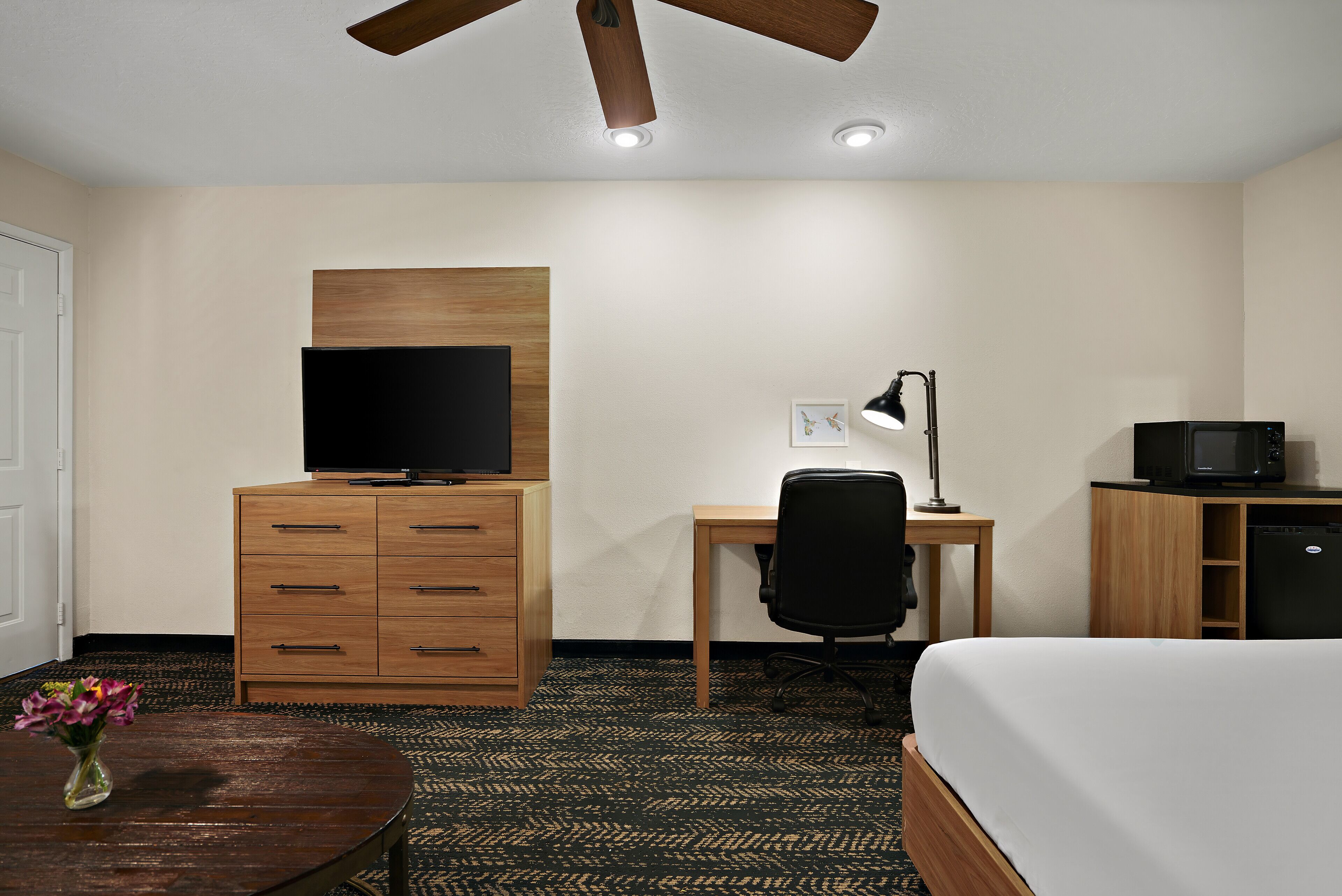 A hotel room with a bed, a desk, a television, a lamp, and a wooden dresser.
