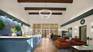A modern hotel lobby with a blue reception desk, wooden flooring, and comfortable seating areas. - La Fuente Inn & Suites (Yuma)