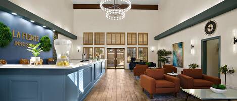 A modern hotel lobby with a blue reception desk, wooden flooring, and comfortable seating areas.
