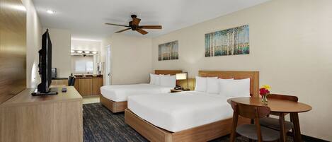 A hotel room with two beds, a desk, a chair, a television, a ceiling fan, and artwork on the walls.