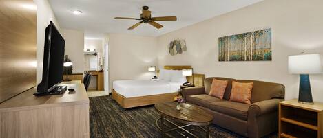 A hotel room with a bed, a sofa, a desk, a television, and a ceiling fan.