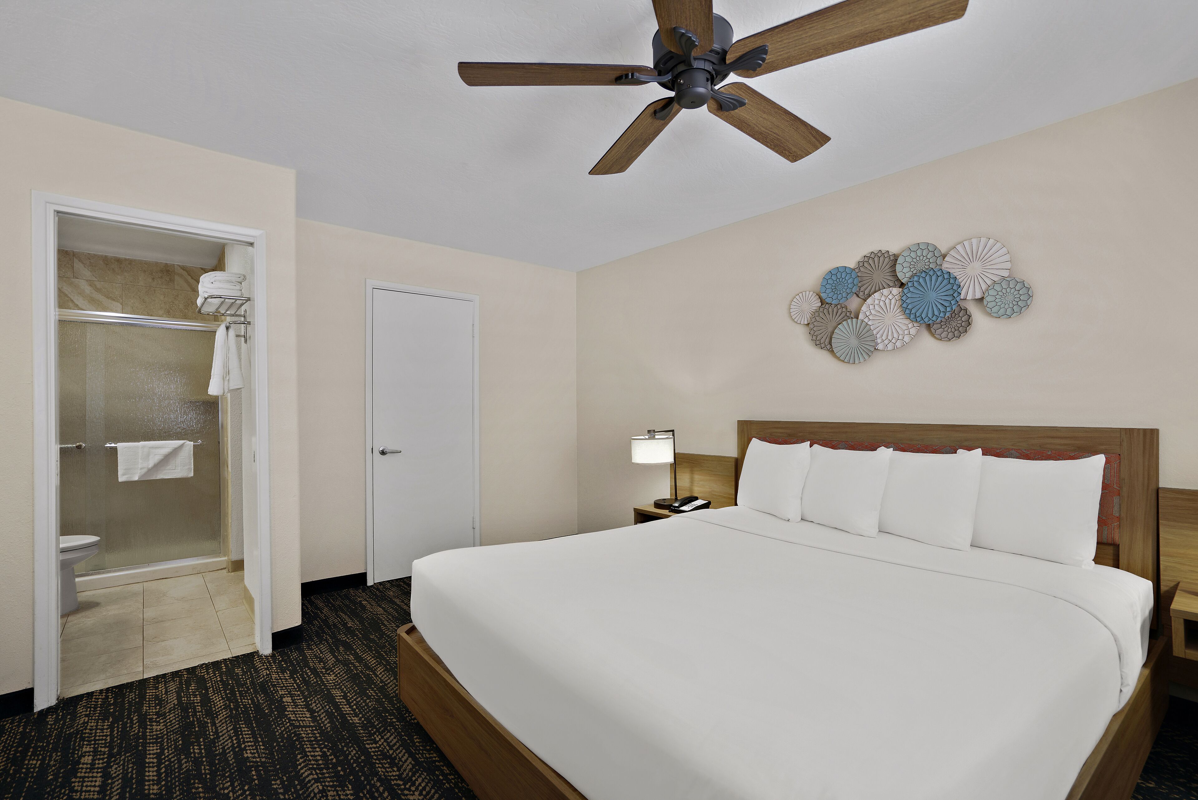 A hotel room with a bed, a ceiling fan, a shower, and a wall decoration.