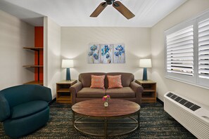 Relax in a cozy space with a comfortable sofa, armchair, and coffee table, complemented by a ceiling fan and artwork.