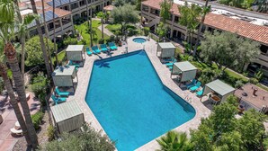 A large rectangular pool with lounge chairs and umbrellas, surrounded by palm trees and a building with a red-tiled roof. - La Fuente Inn & Suites (Yuma)