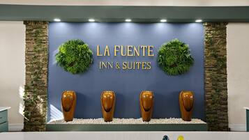 A reception area with a sign reading "LA FUENTE INN & SUITES" and three wooden sculptures.