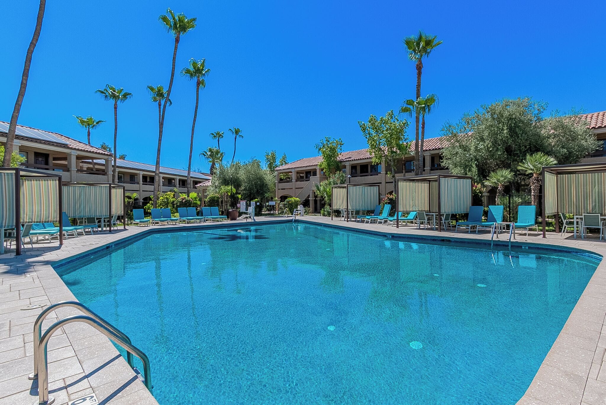 A swimming pool with lounge chairs, palm trees, and a building with a tiled roof.