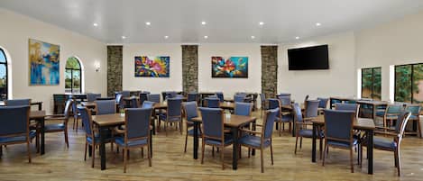 A spacious dining area with multiple tables and chairs, stone accents on the walls, and a flat-screen TV mounted above the tables.