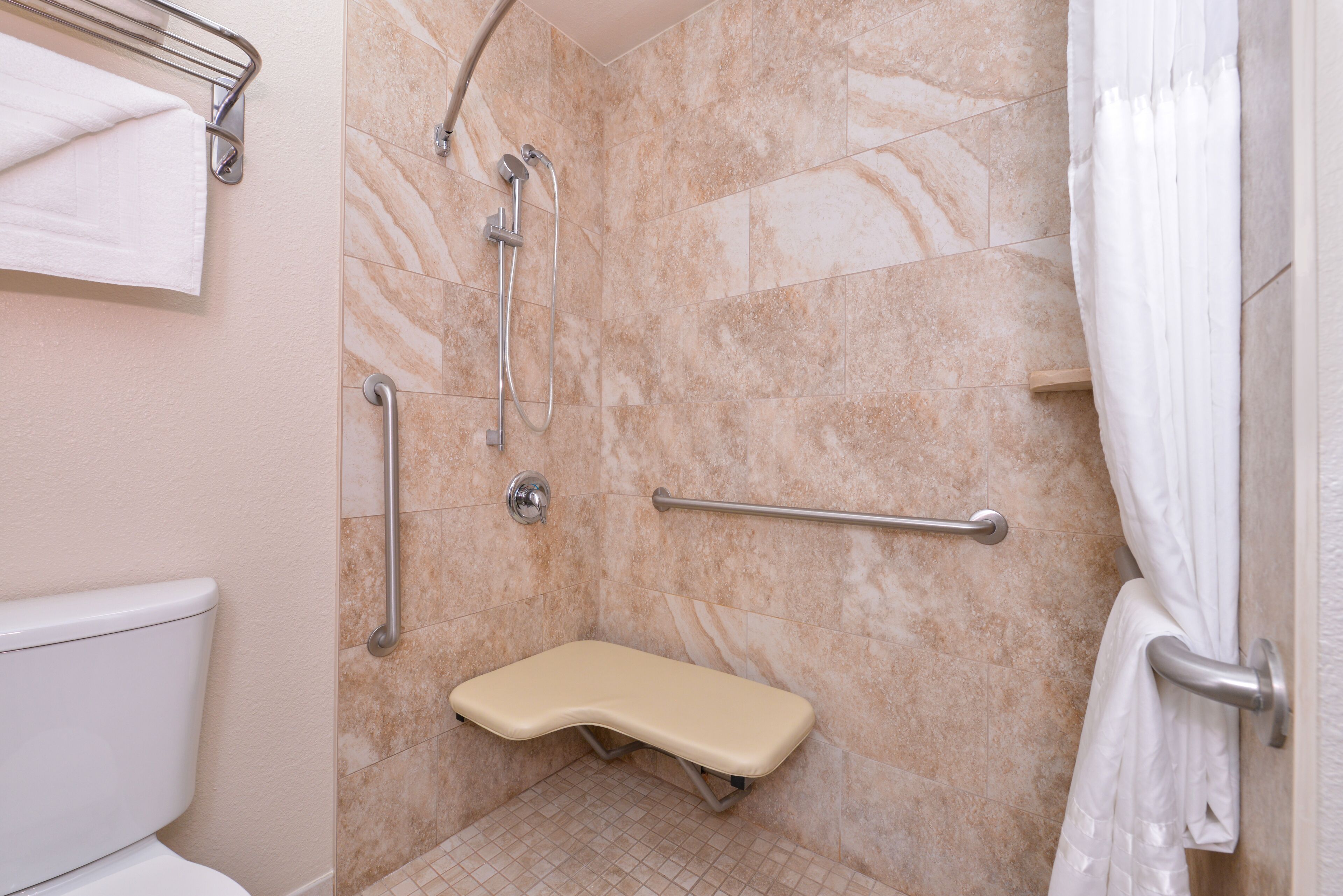 A bathroom with a shower, grab bars, a toilet, and a bench.