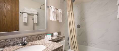 A bathroom with a granite countertop sink, a mirror, a toilet, a shower with a beige curtain, and a marble wall.