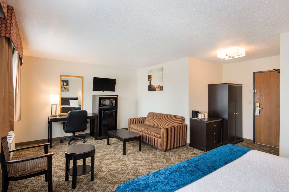 A hotel room with a bed, a desk with a computer, a chair, a sofa, a TV, and a wardrobe.
