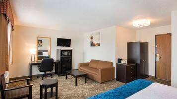 A hotel room with a bed, a desk with a computer, a chair, a sofa, a TV, and a wardrobe.