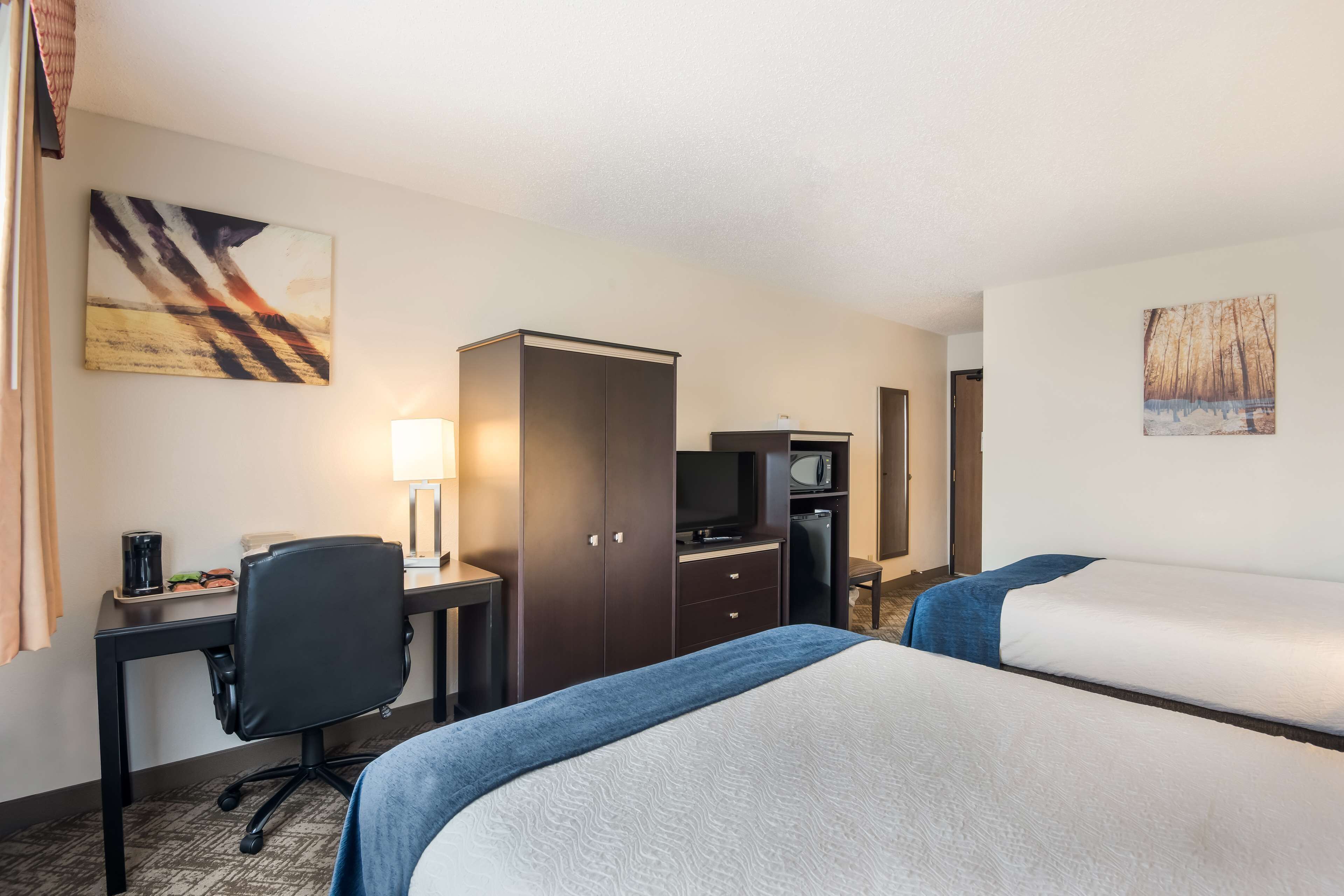 A hotel room with two beds, a desk with a chair, a television, and a wardrobe.