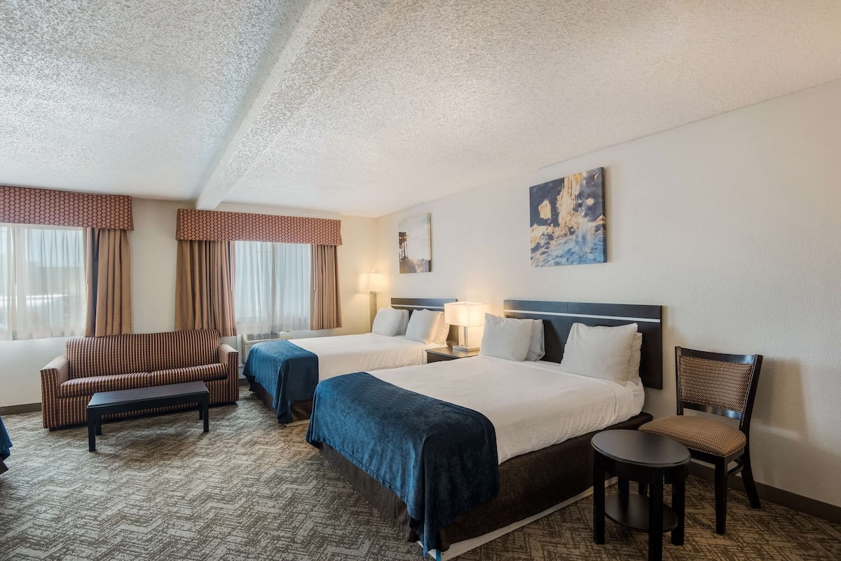 A hotel room with two beds, a sofa, a chair, a small table, and a painting on the wall.